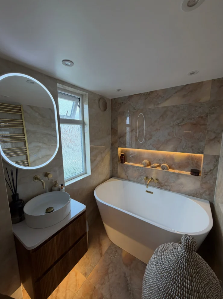 A bathroom fitted by Elegance: marble-effect tiles, freestanding bath, lit niche and brass taps